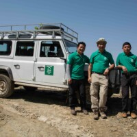 Three Gurkha Welfare Trust staff members dressed in green next to a Gurkha Welfare Trust land rover